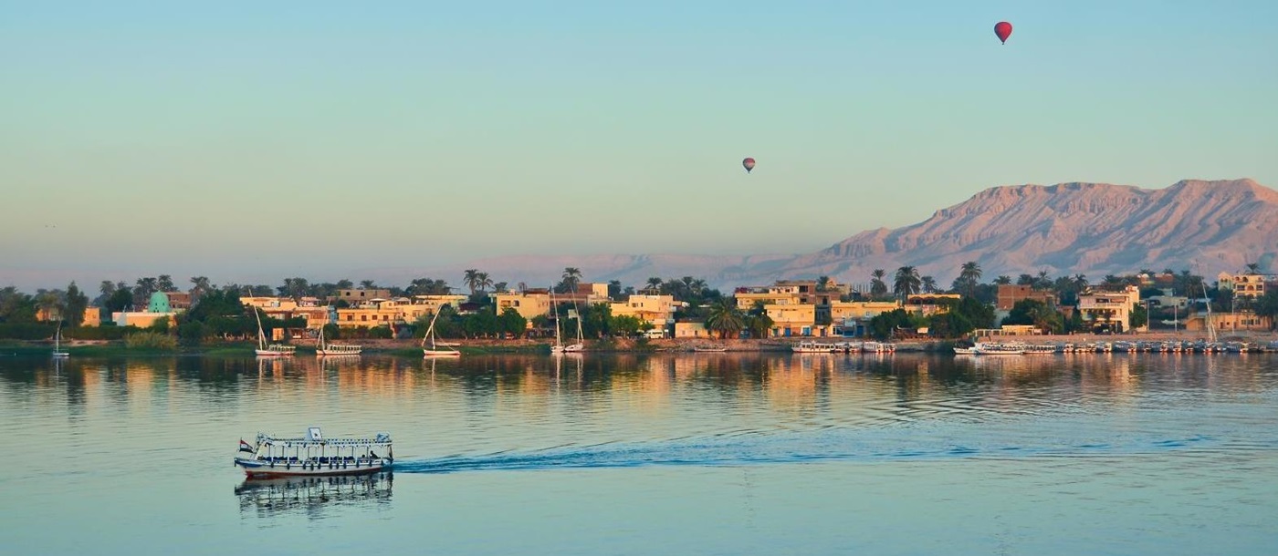 A small cruise ship on the River Nile with the Valley of the Kings in the background