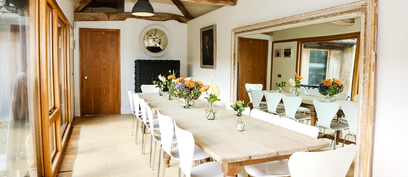 Dining area with big feature mirror and view over the courtyard at English luxury villa Temple Guiting Barn
