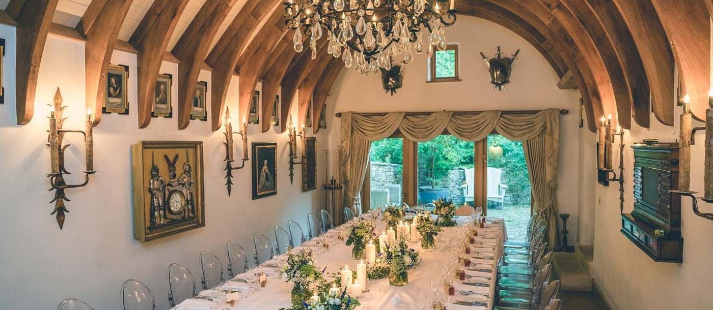 Dining room with set long table, chairs, paintings and chandelier at Temple Guiting Manor in the Cotswolds, England