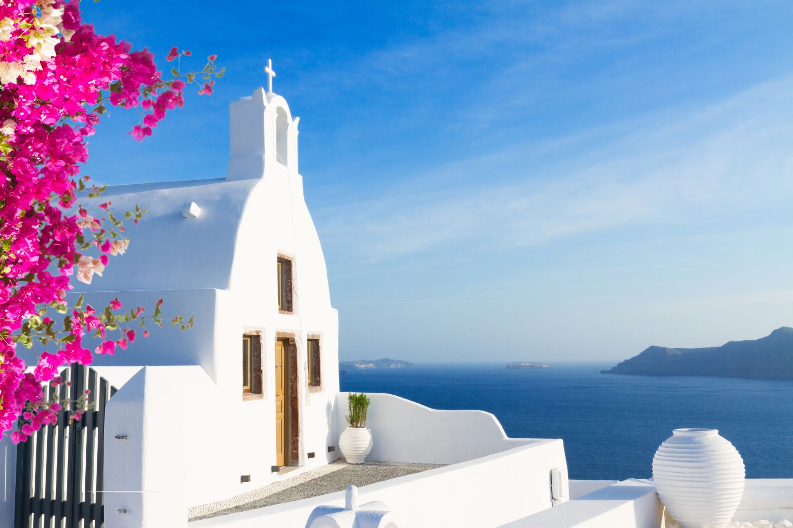 Pink bougainvillea and white chapel facing out to sea in Santorini