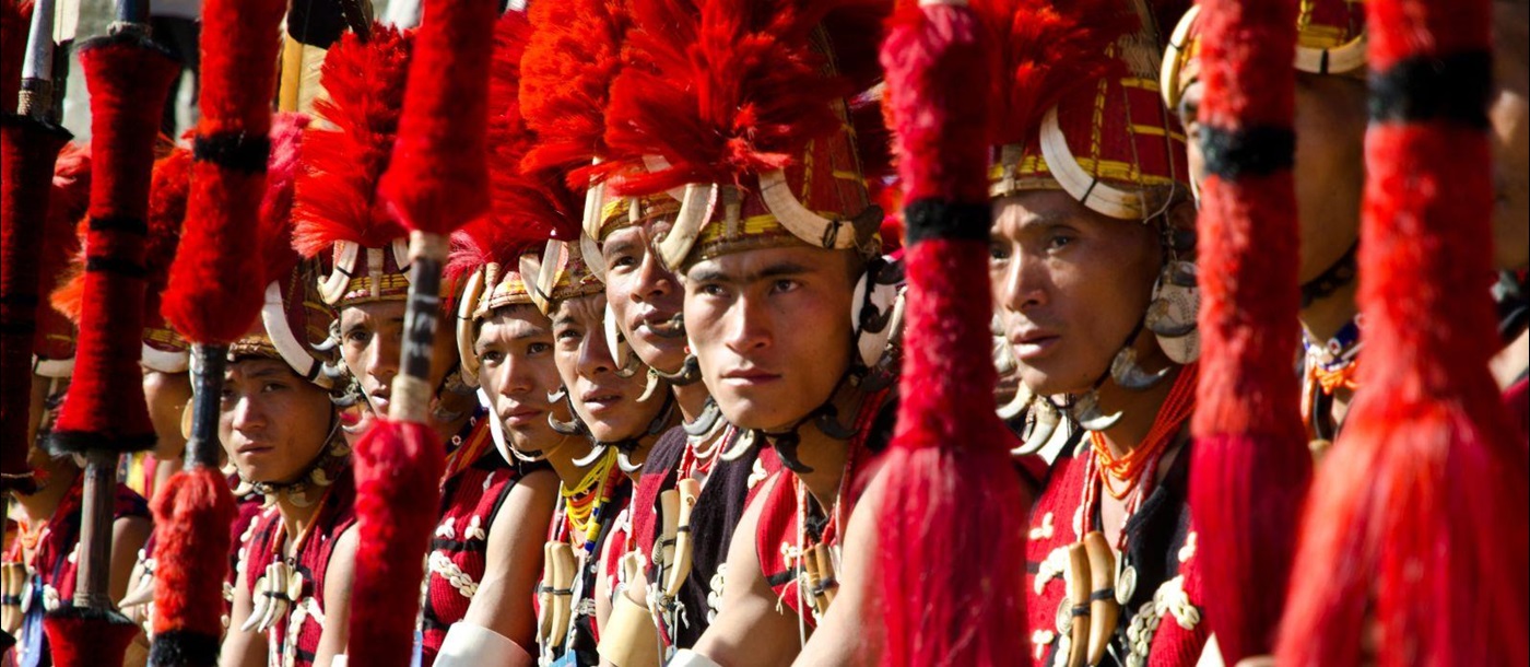 A row of men from the Tribes of Nagaland dressed in traditional red headdress and holding spears at the annual Hornbill Festival in India