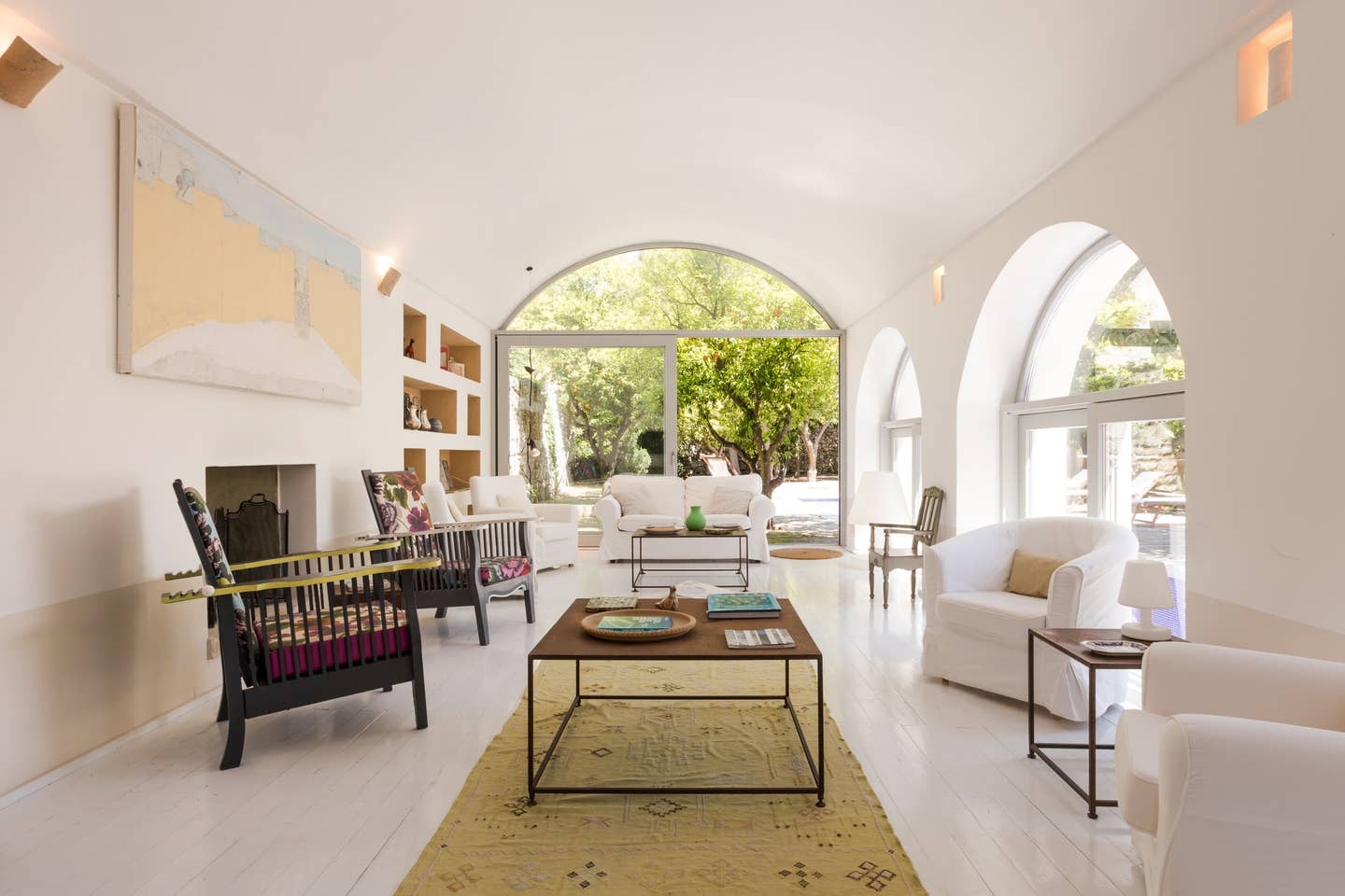 Living room with sofa, 6 armchairs, coffee tables, painting, shelves and patio doors at Palazzo del Duca in Puglia, Italy