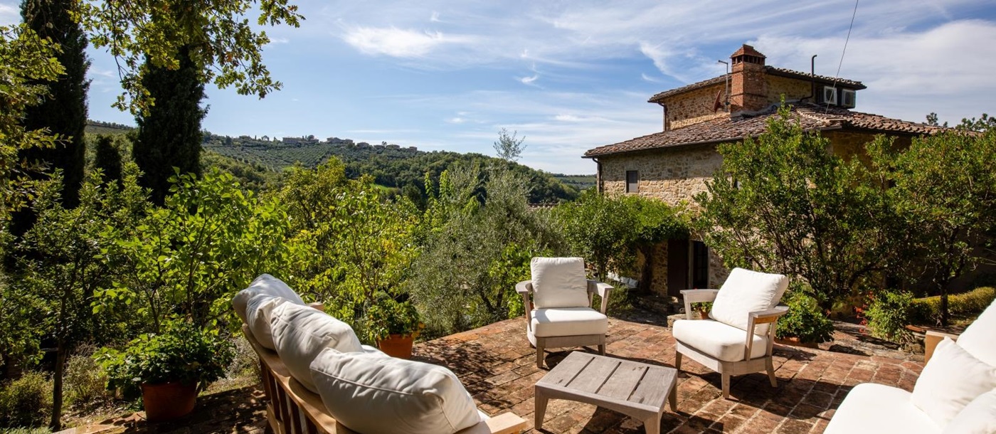 Patio with comfy chairs, coffee table and countryside view at the back of Villa Baciata in Tuscany, Italy