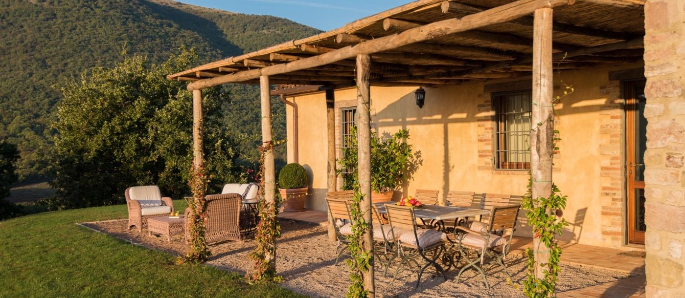 Patio with covered dining area, table, chairs, fruit, plants, comfy chairs and mountain view at Bel Canto in Umbria, Italy