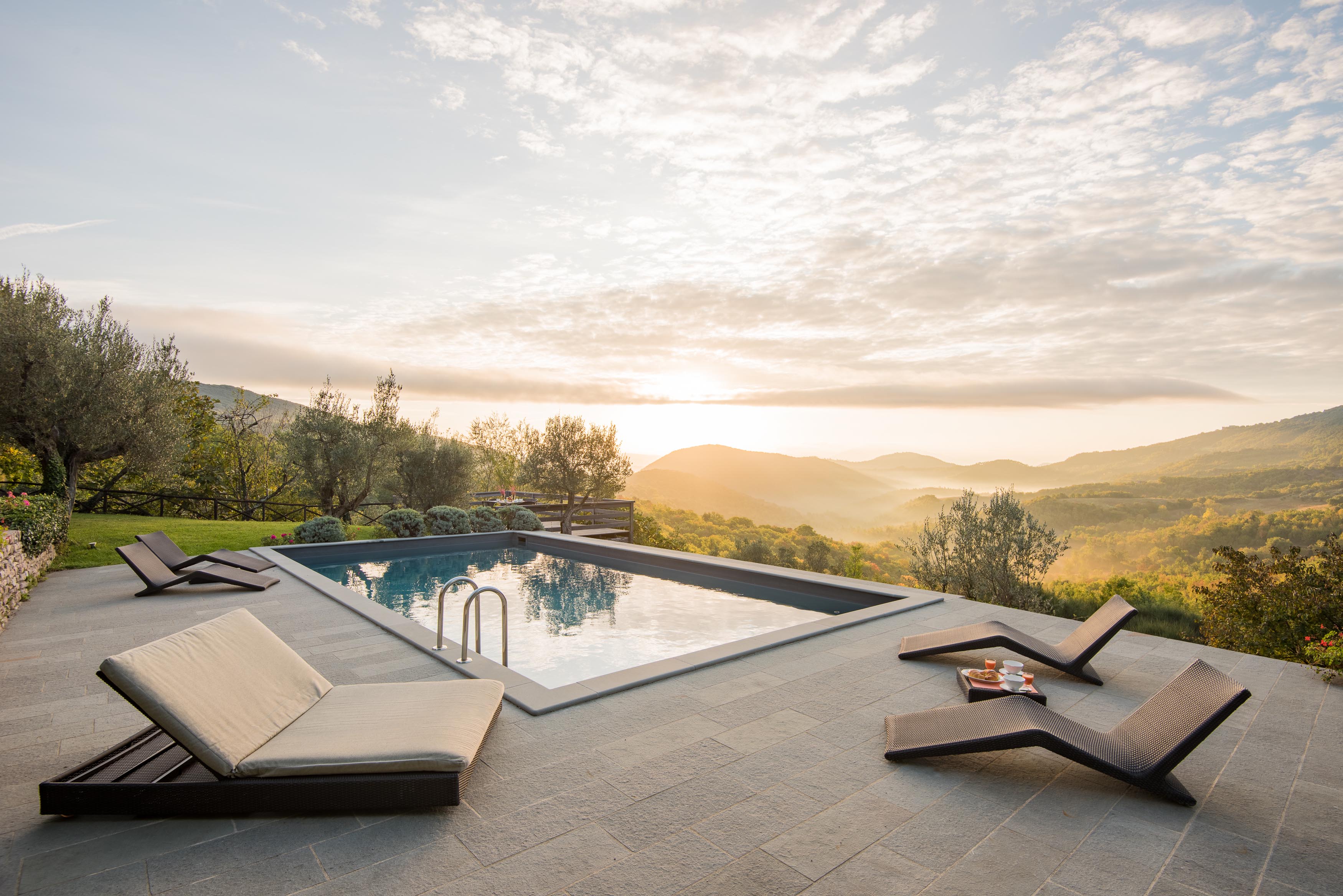 Pool area with patio, sun loungers, food, drink, grass & view of balcony and countryside at Villa Pizzicato in Umbria, Italy