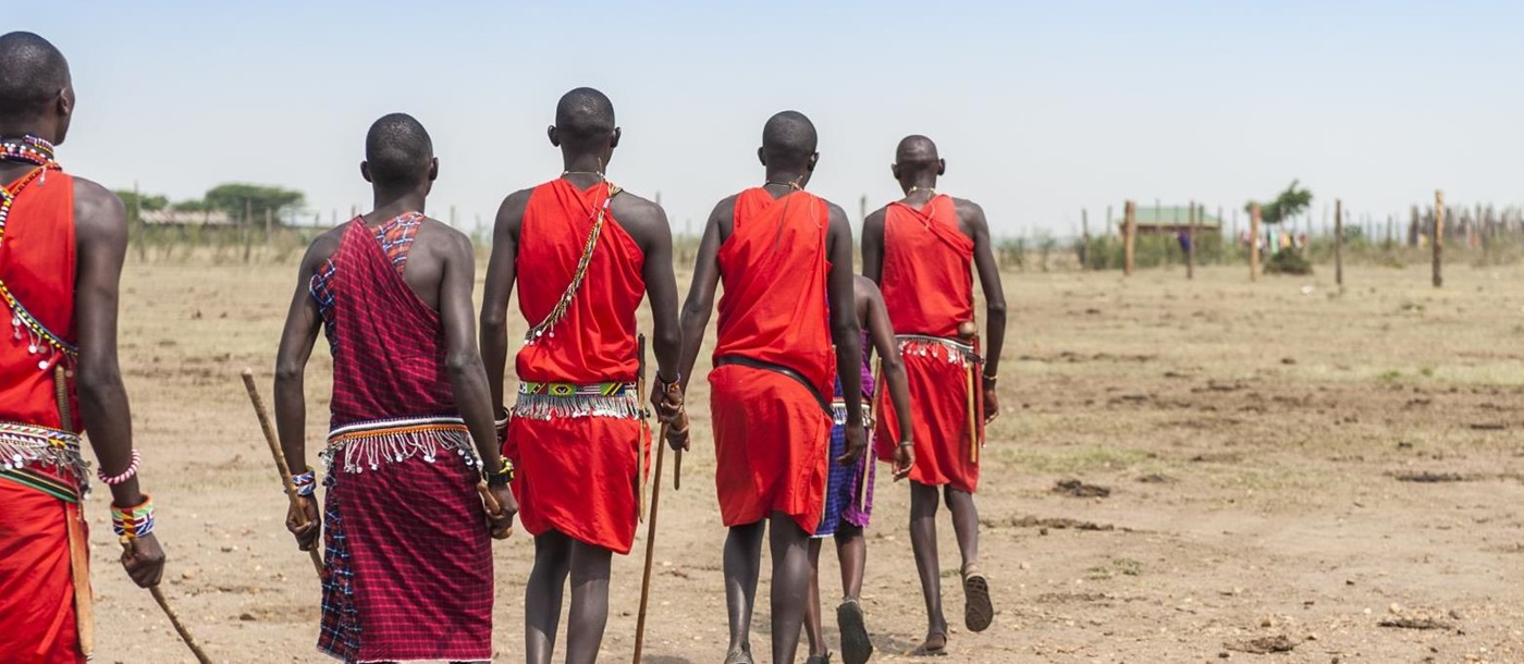 Masai warriors in traditional red dress walking through the plains in Kenya