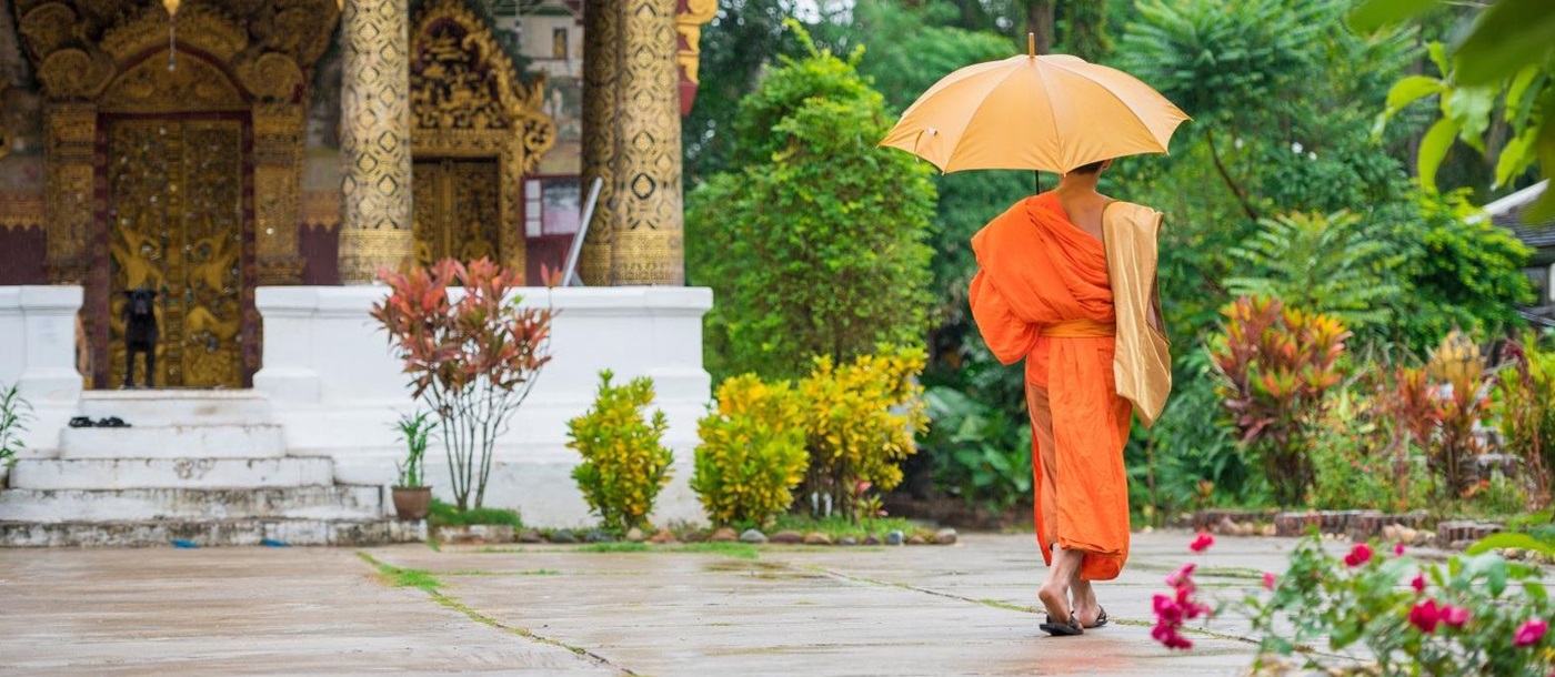 Buddhist monk in traditional dress approaching a temple in Laos
