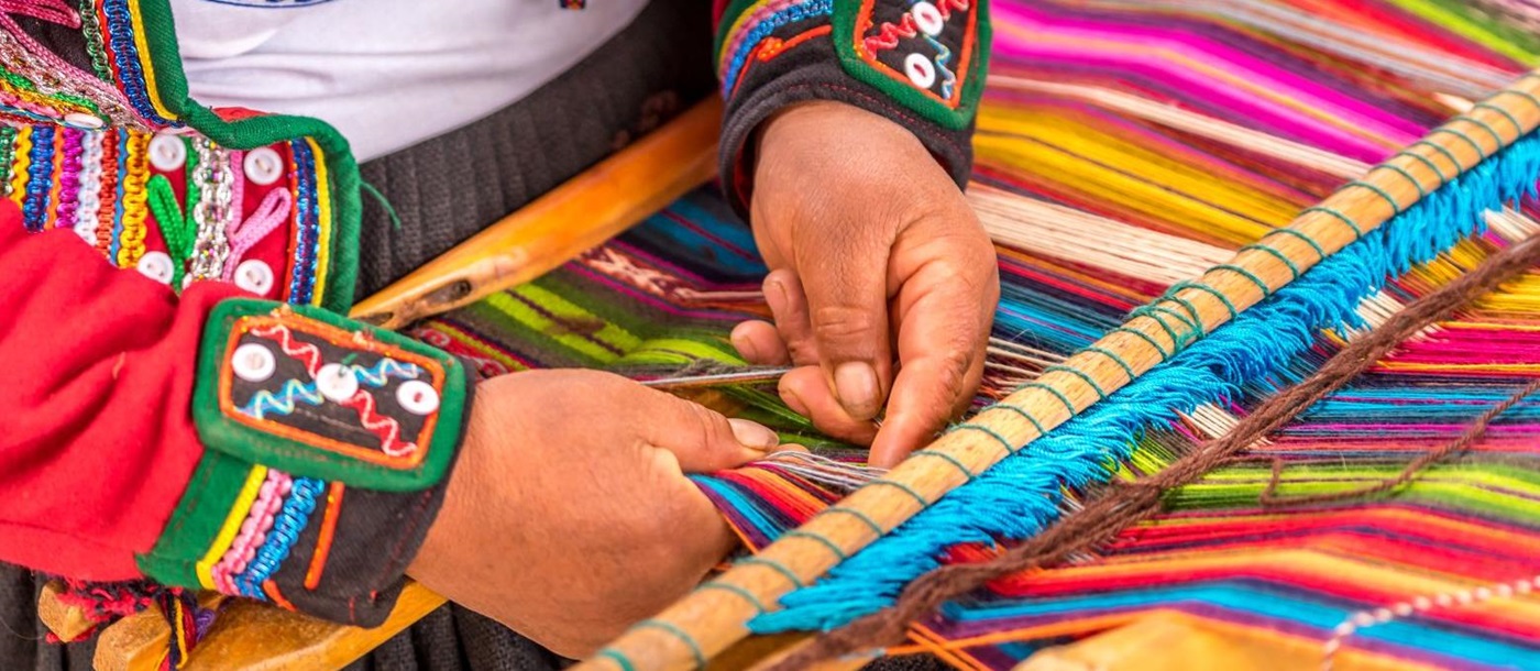 Peruvian lady in traditional dress weaving colourful textiles in the Sacred Valley of the Incas