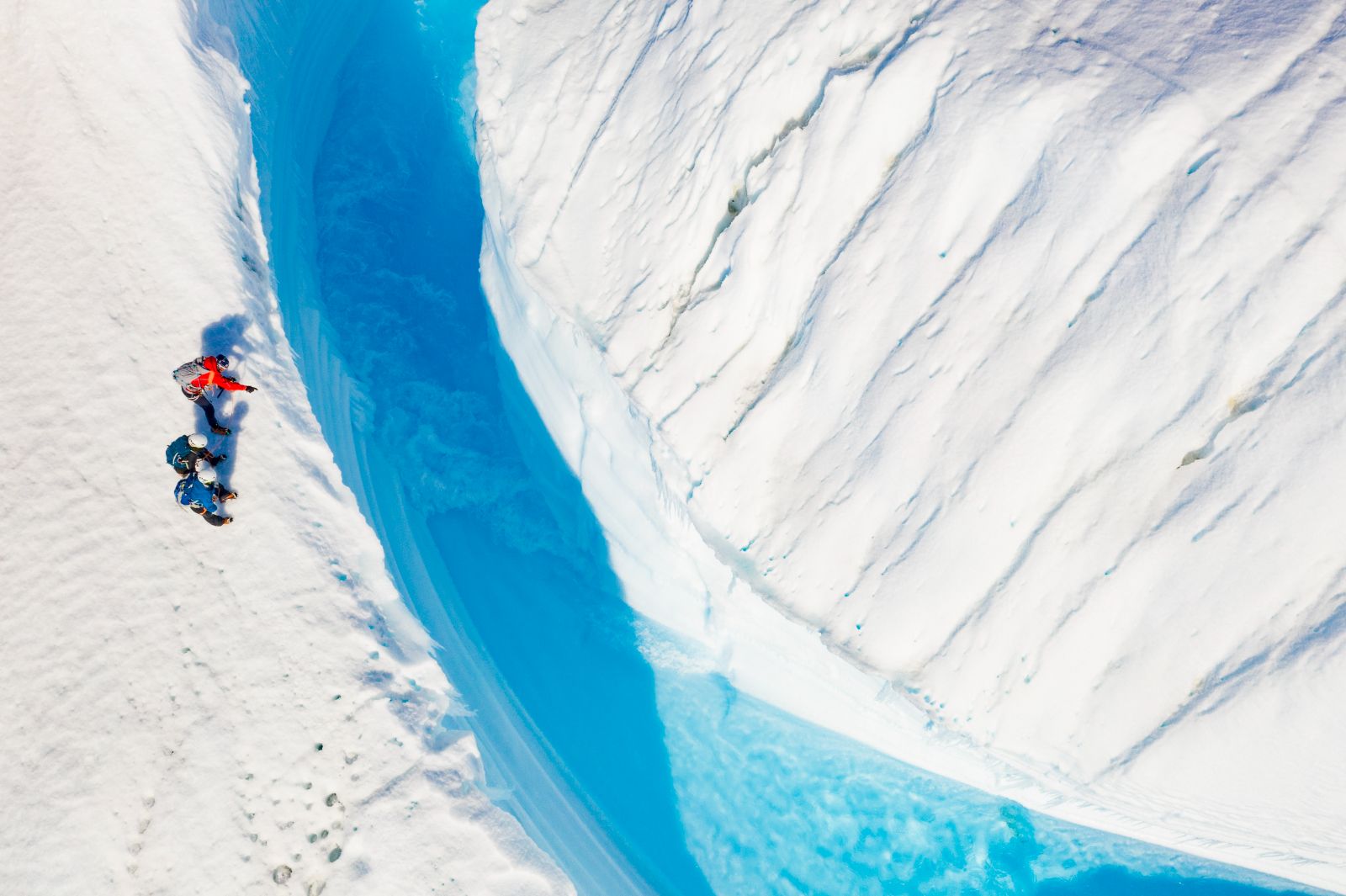People trekking along a large ice crevasse in Antarctica