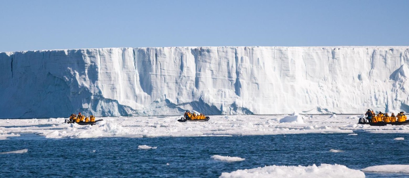 Three Zodiacs at the face of an enormous tabular iceberg in Svalbard Norway