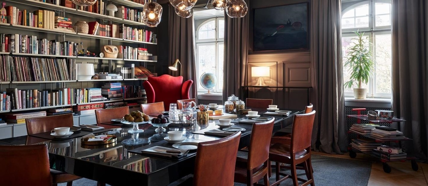 Dining room set for brakfast with big windows and a wall-covering book shelf