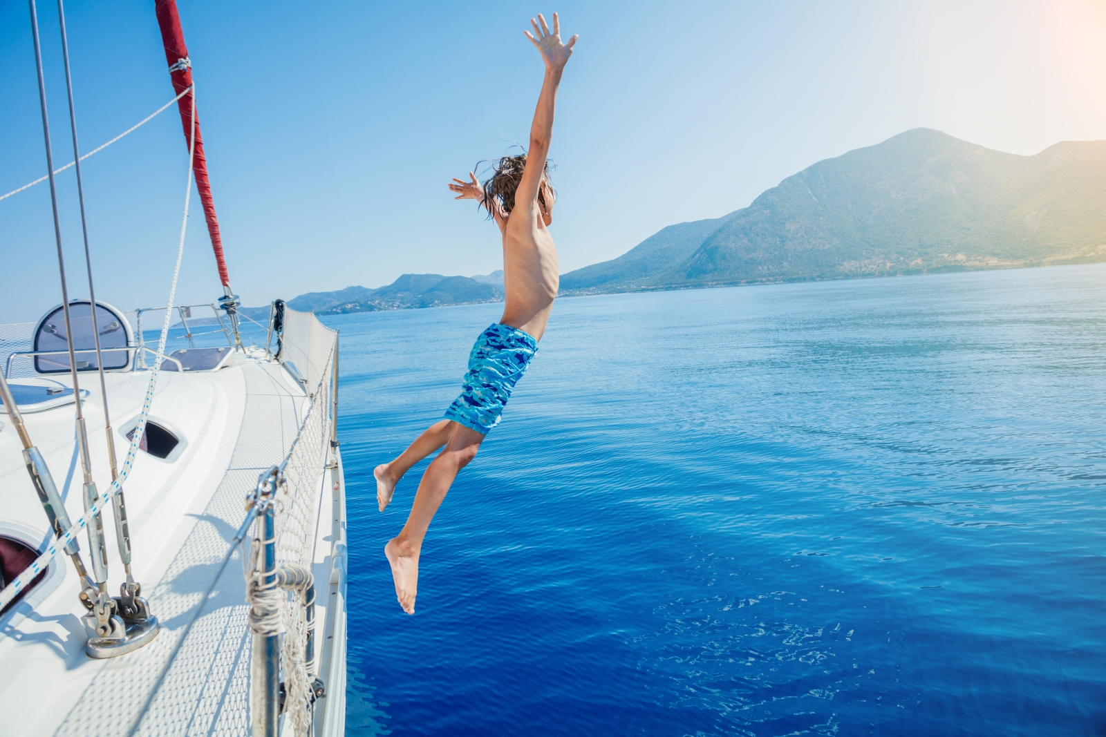 boy jumping of a sailing boat into blue water