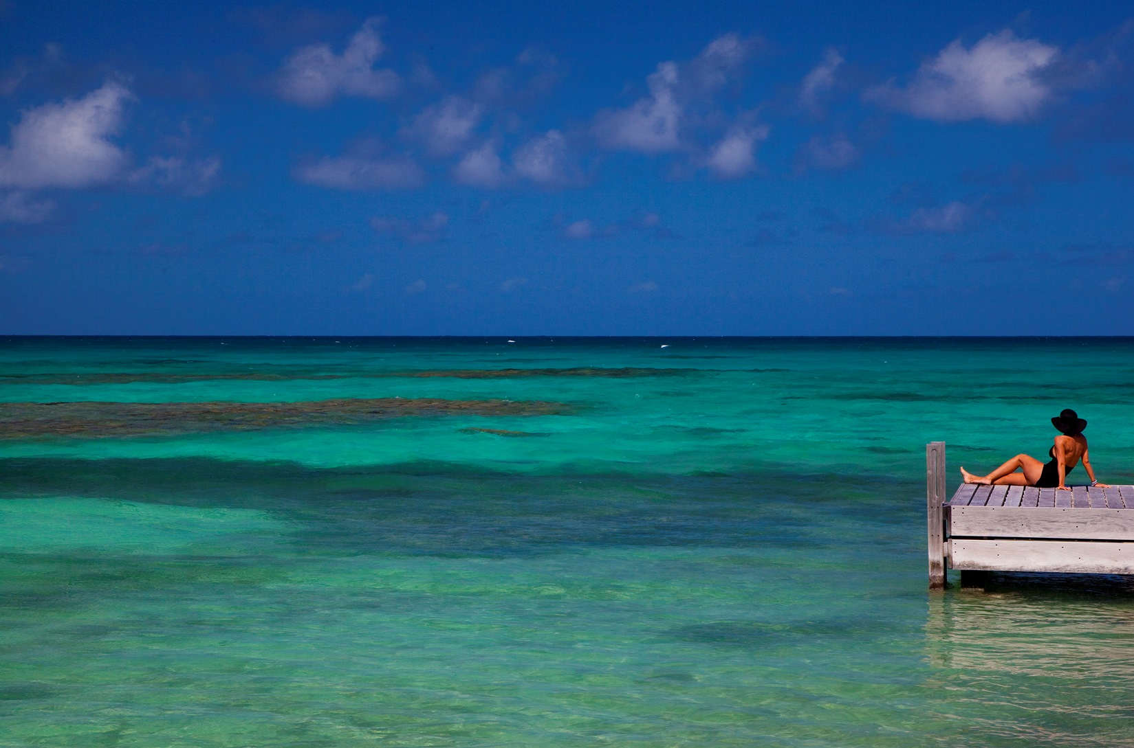 A woman sitting on a pier while watching the ocean near Frangipani, Antigua