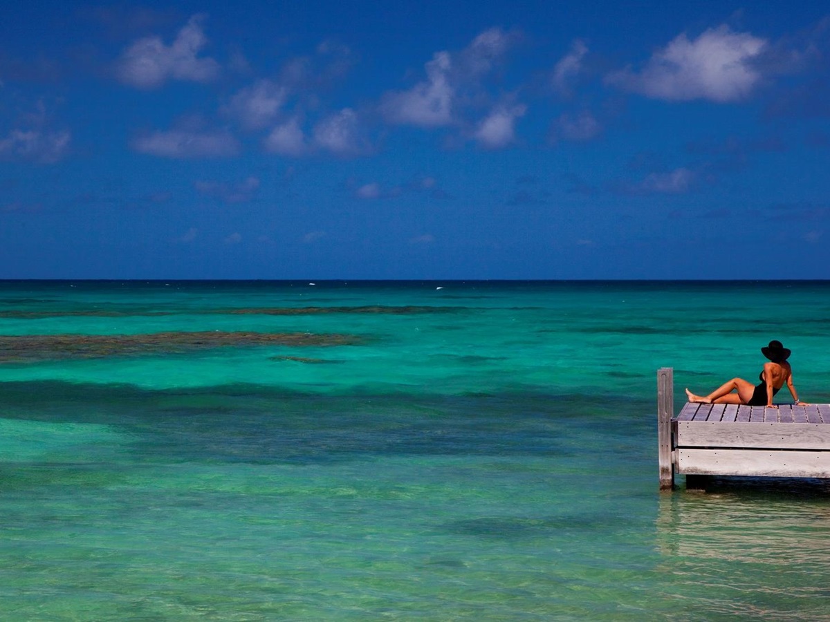 A woman sitting on a pier while watching the ocean near Frangipani, Antigua