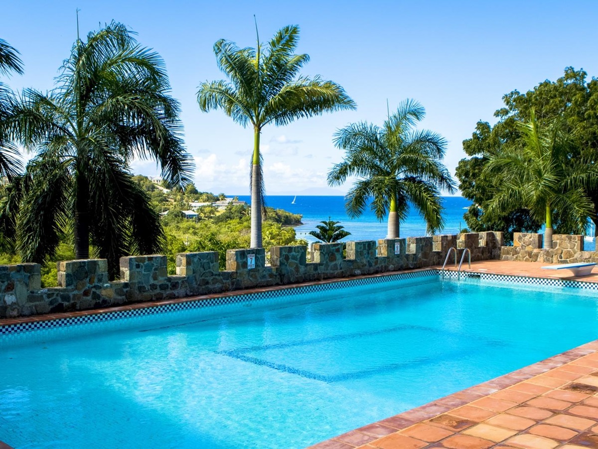 Pool and pool area with diving board, palm trees and sea view at St Anne’s Point in Antigua, the Caribbean