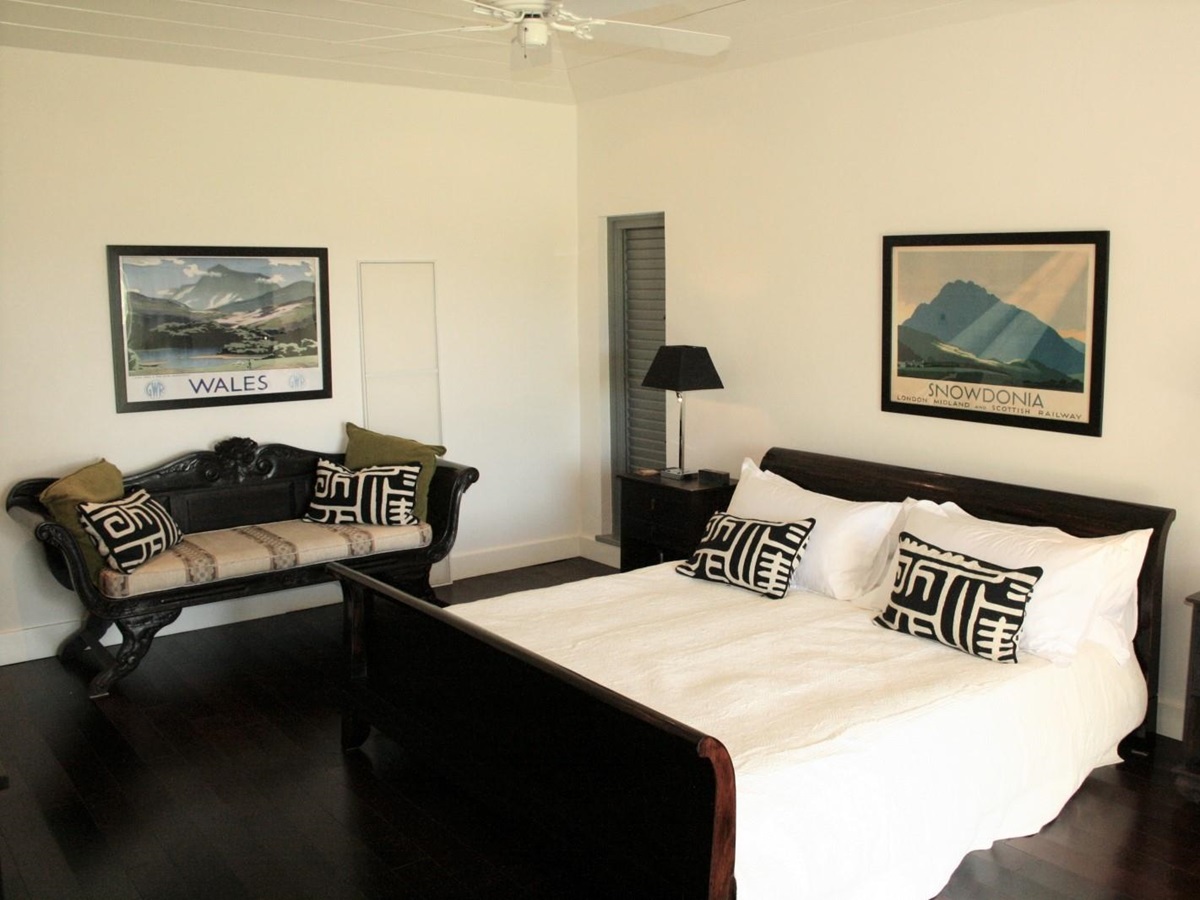 Bedroom with double bed, bedside tables, lamps, sofa and vintage artwork at The Hill Club in Antigua, the Caribbean