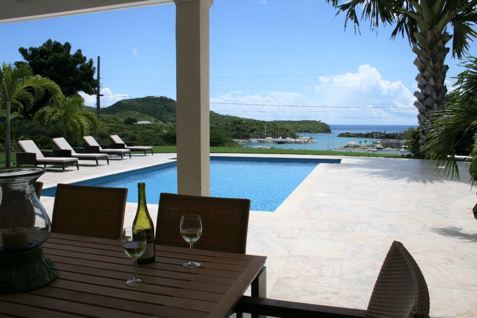 Outdoor dining area with table, chairs, wine, candle and view of pool & harbour at The Hill Club in Antigua, the Caribbean