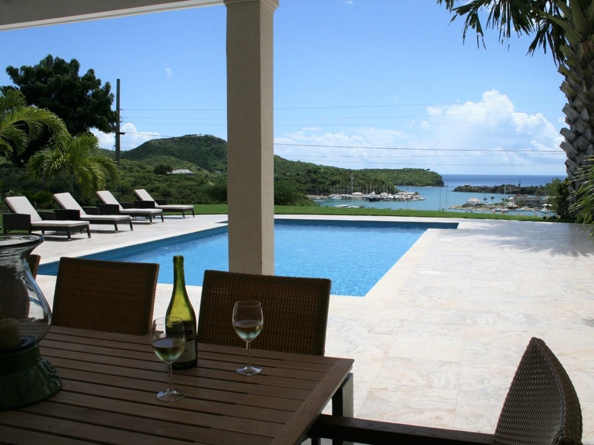 Outdoor dining area with table, chairs, wine, candle and view of pool & harbour at The Hill Club in Antigua, the Caribbean