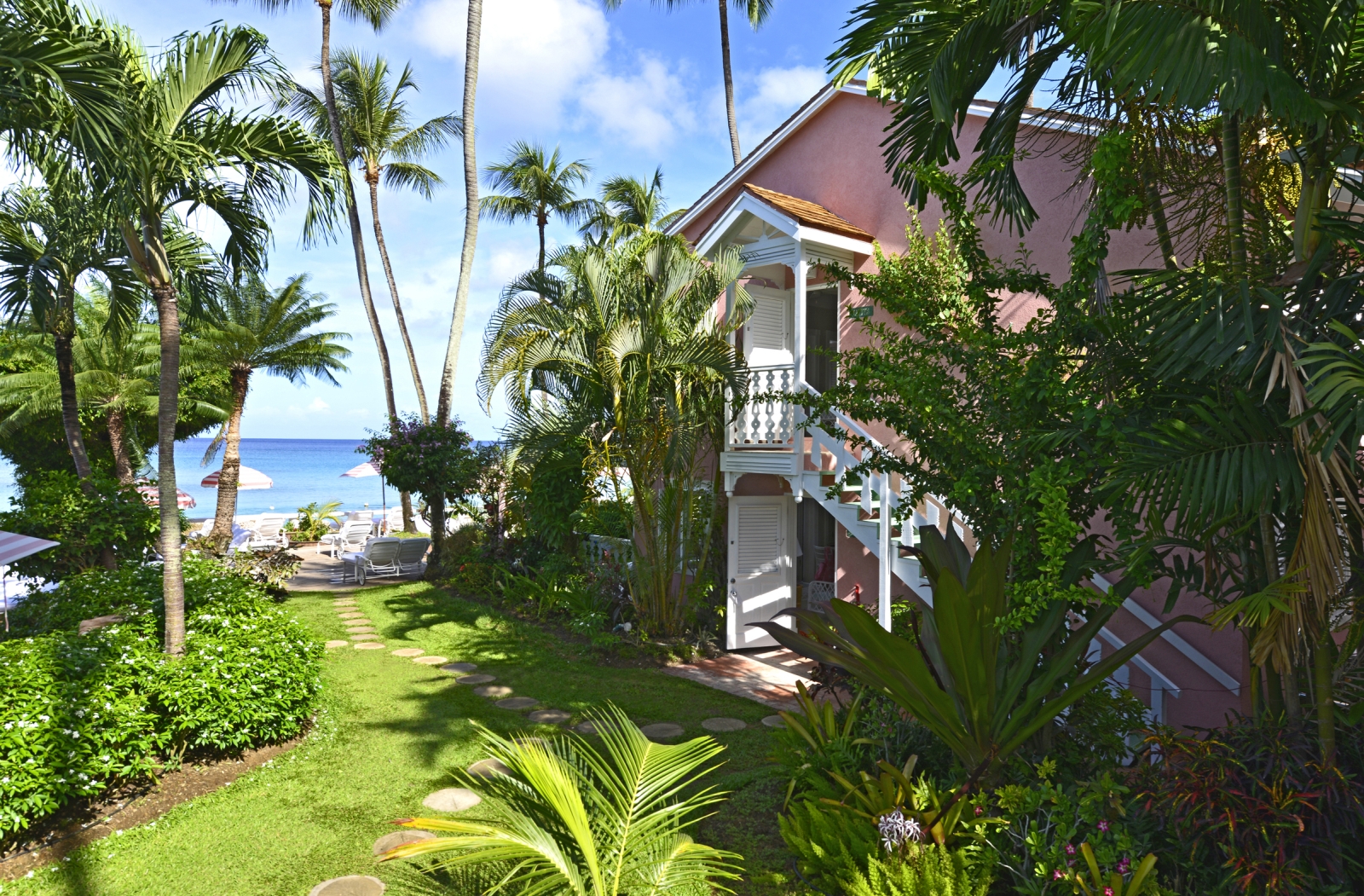 Pink house in lush green gardens with ocean in the background