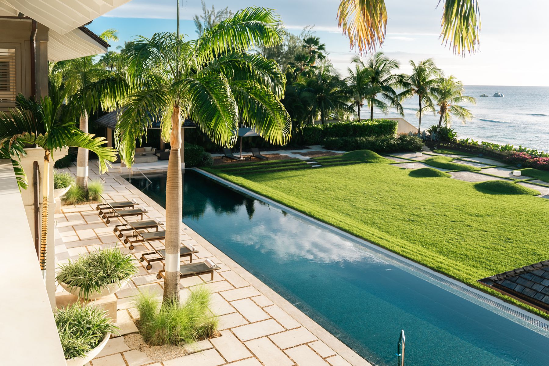 Pool with palm trees and sunbeds looking out to sea at Godings Beach House in Barbados