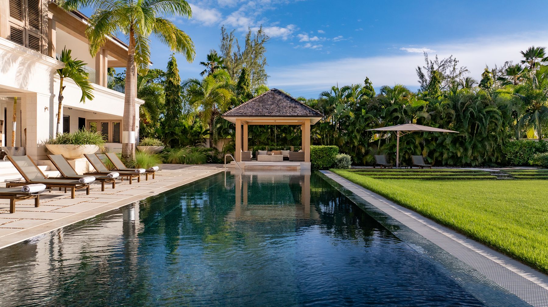 Pool with palm trees and sunbeds looking out to sea at Godings Beach House in Barbados