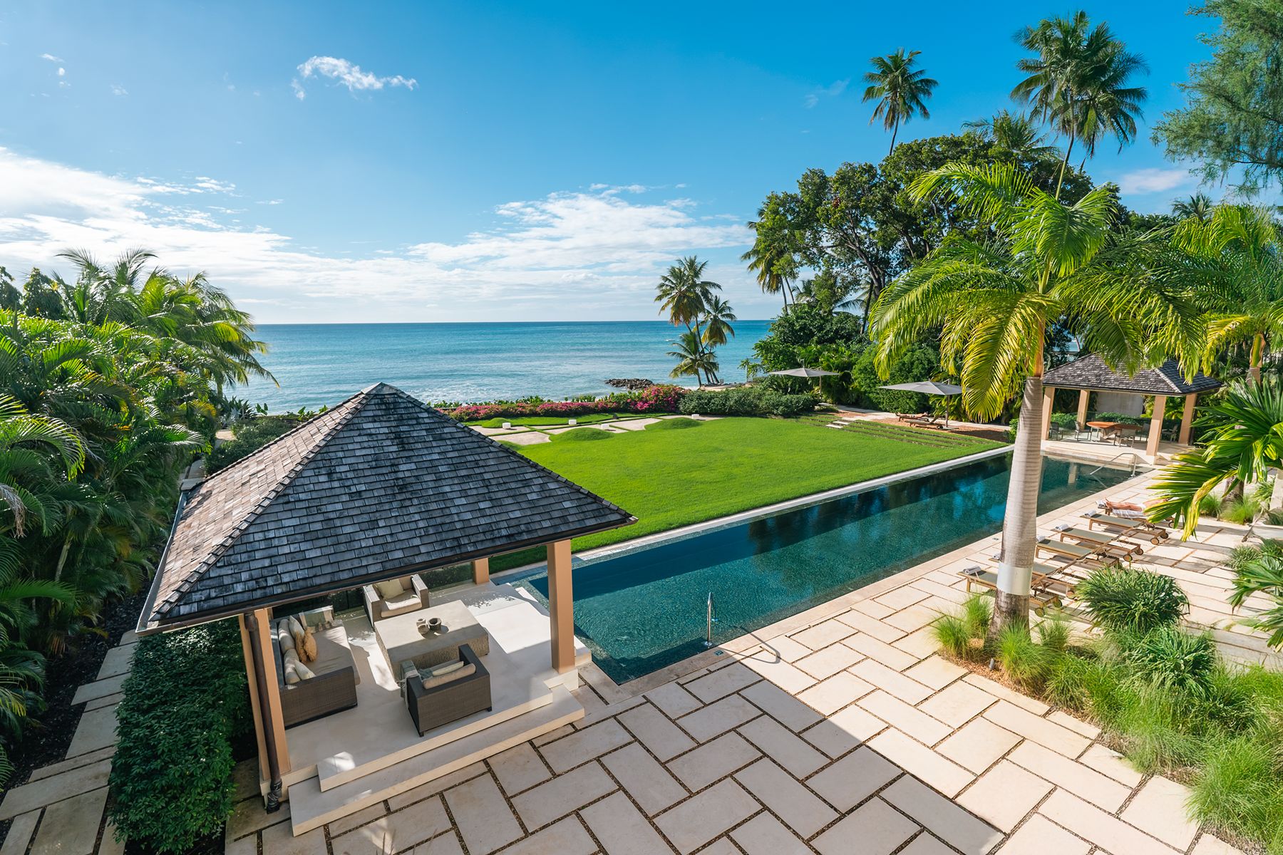 Pool hut and pool with palm trees and sunbeds looking out to sea at Godings Beach House in Barbados