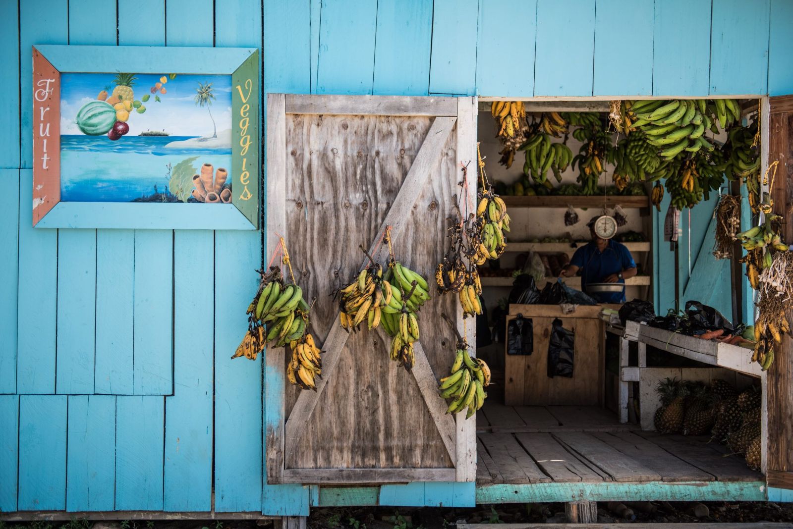 Local store front in Placencia with vibrant blue wall and fresh bananas, Belize