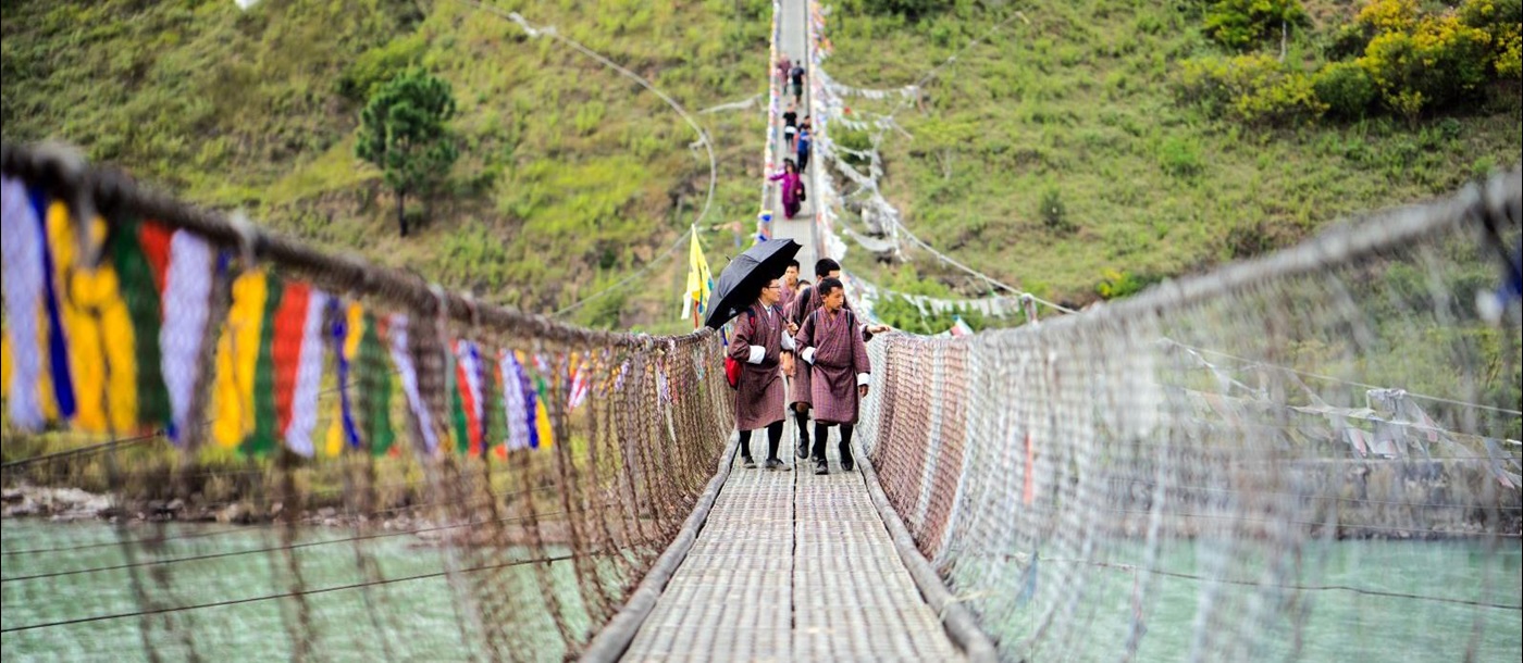 Locals walk towards camera on a bridge crossing the river