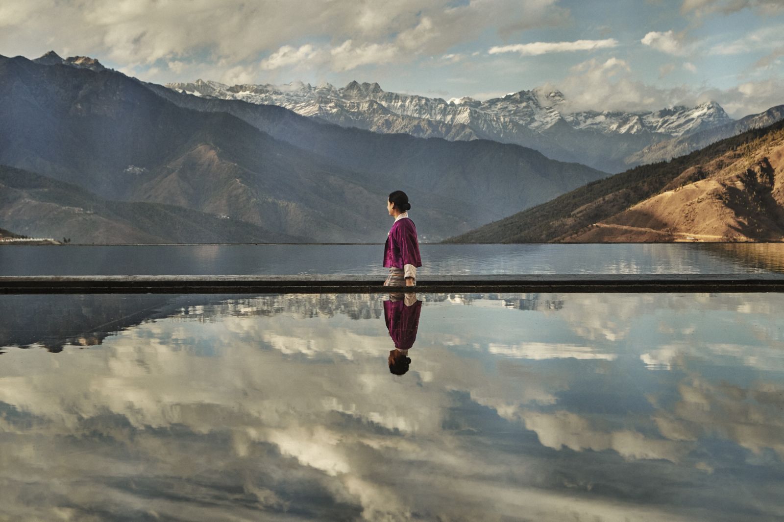 Woman walking in front of a pool reflecting the sky and mountains surrounding luxury hotel Six Senses Thimpu Lodge in Bhutan