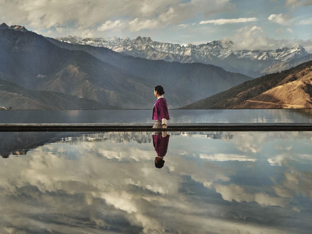 Woman walking in front of a pool reflecting the sky and mountains surrounding luxury hotel Six Senses Thimpu Lodge in Bhutan