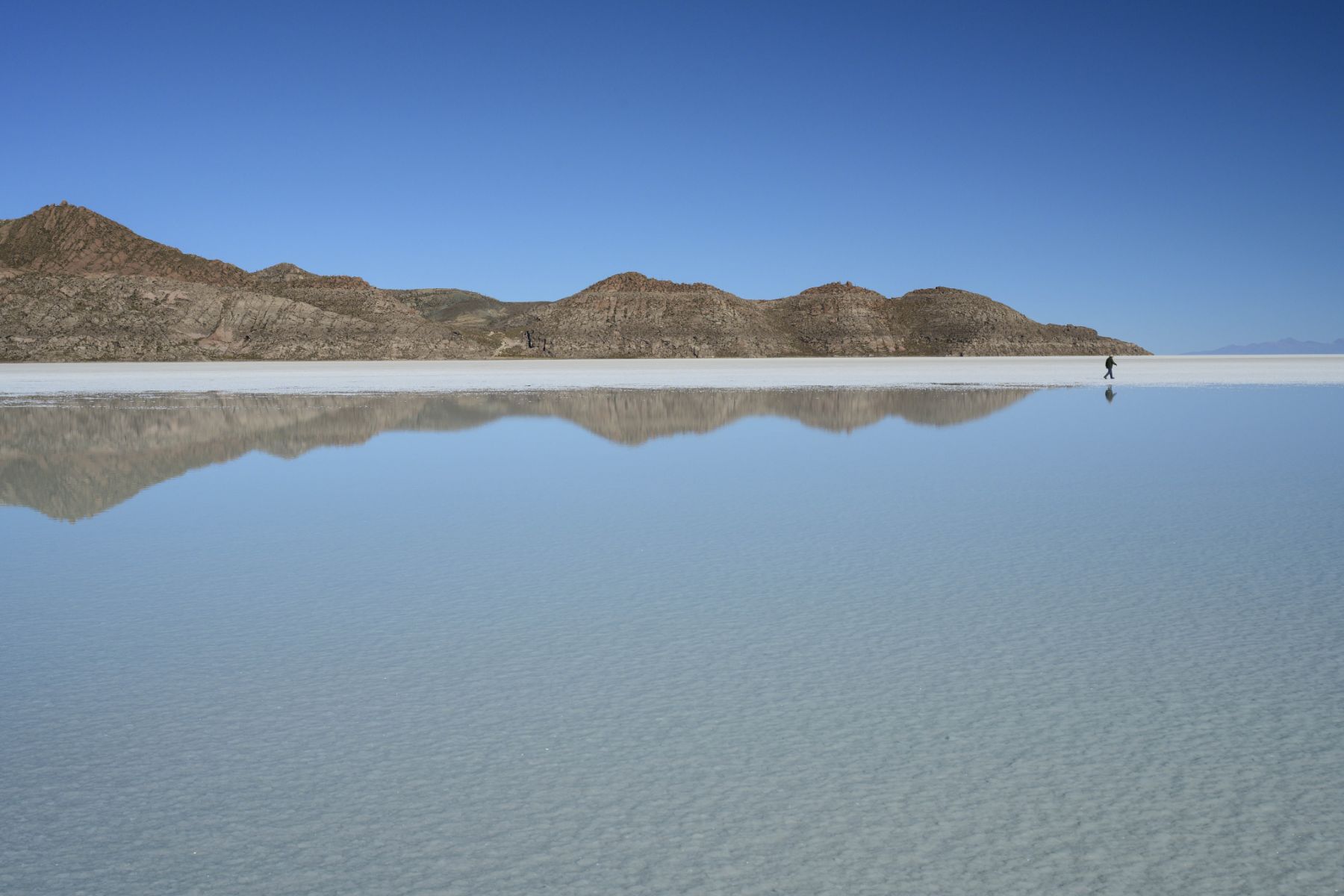 Person walking across the Uyuni salt flat with mountain reflection