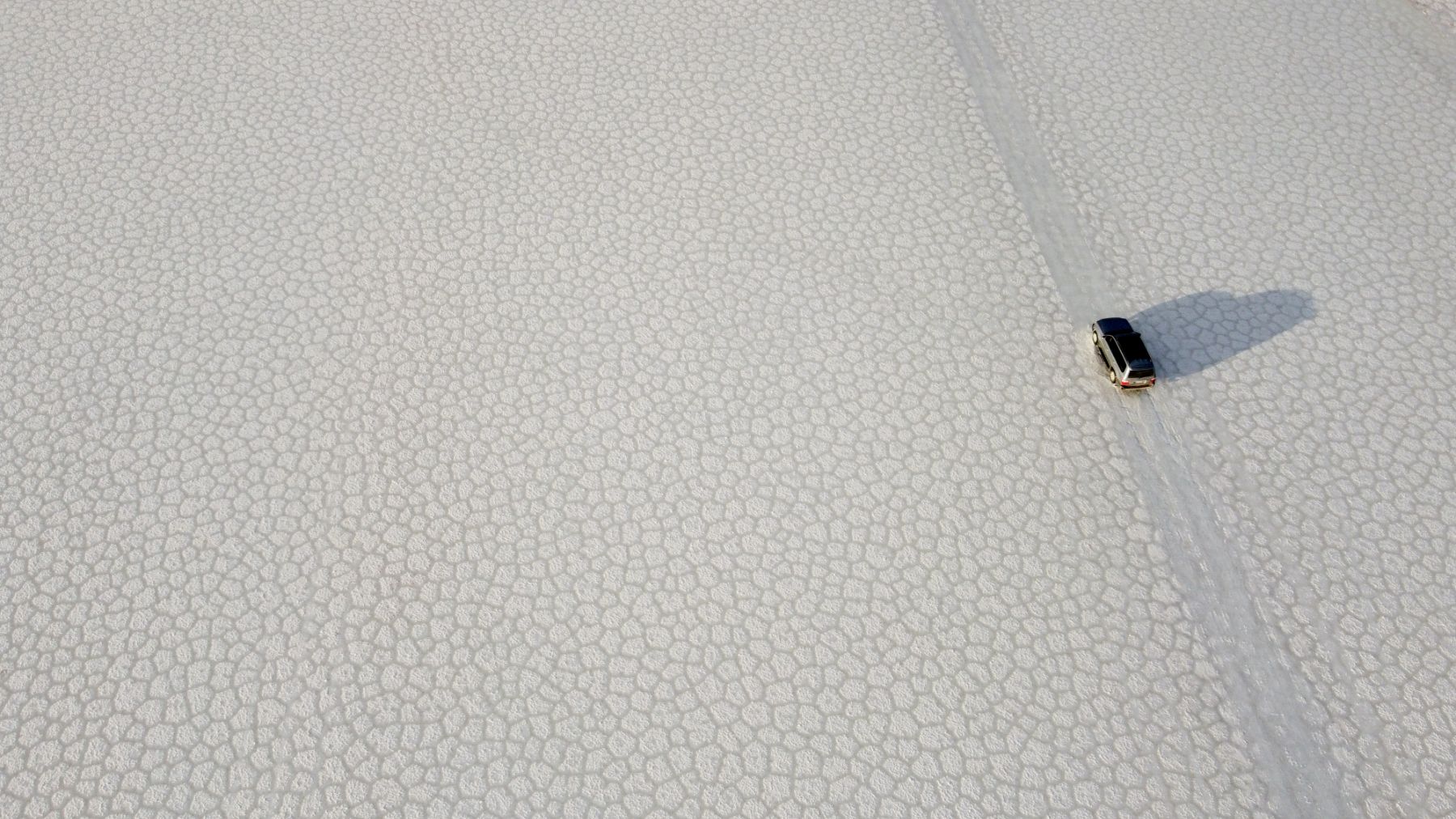 Aerial view of a vehicle driving across the vast white Uyuni salt flat in Bolivia