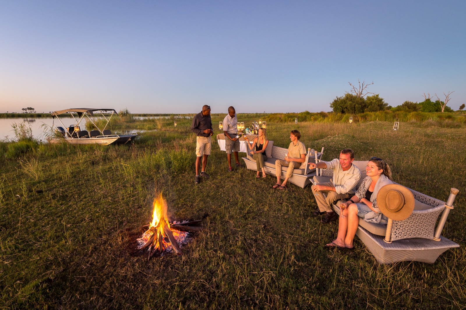 Guests enjoying sundowners with a campfire on safari on the banks of the Okavango in Botswana