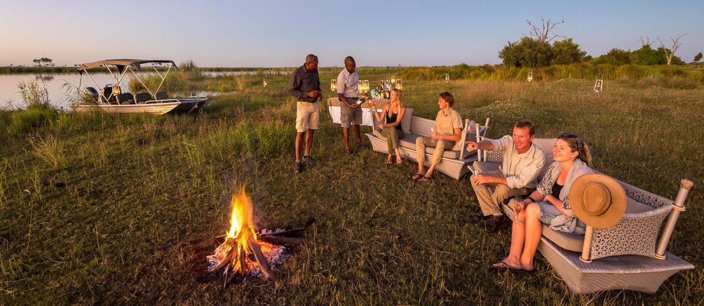 Guests enjoying sundowners with a campfire on the banks of the Okavango