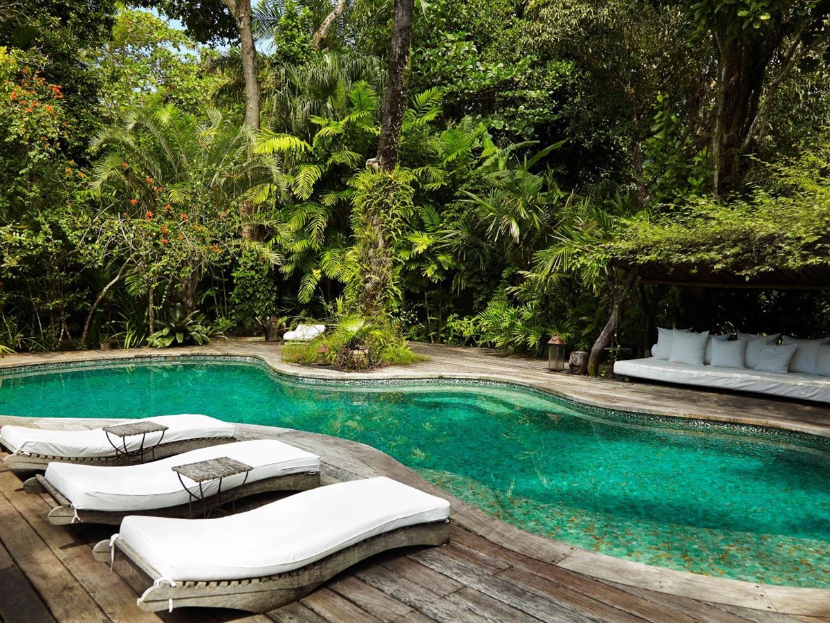 Serene outdoor pool with luxury sunbeds surrounded by tall trees and bushes at luxury resort Uxua Casa Hotel and Spa in Brazil
