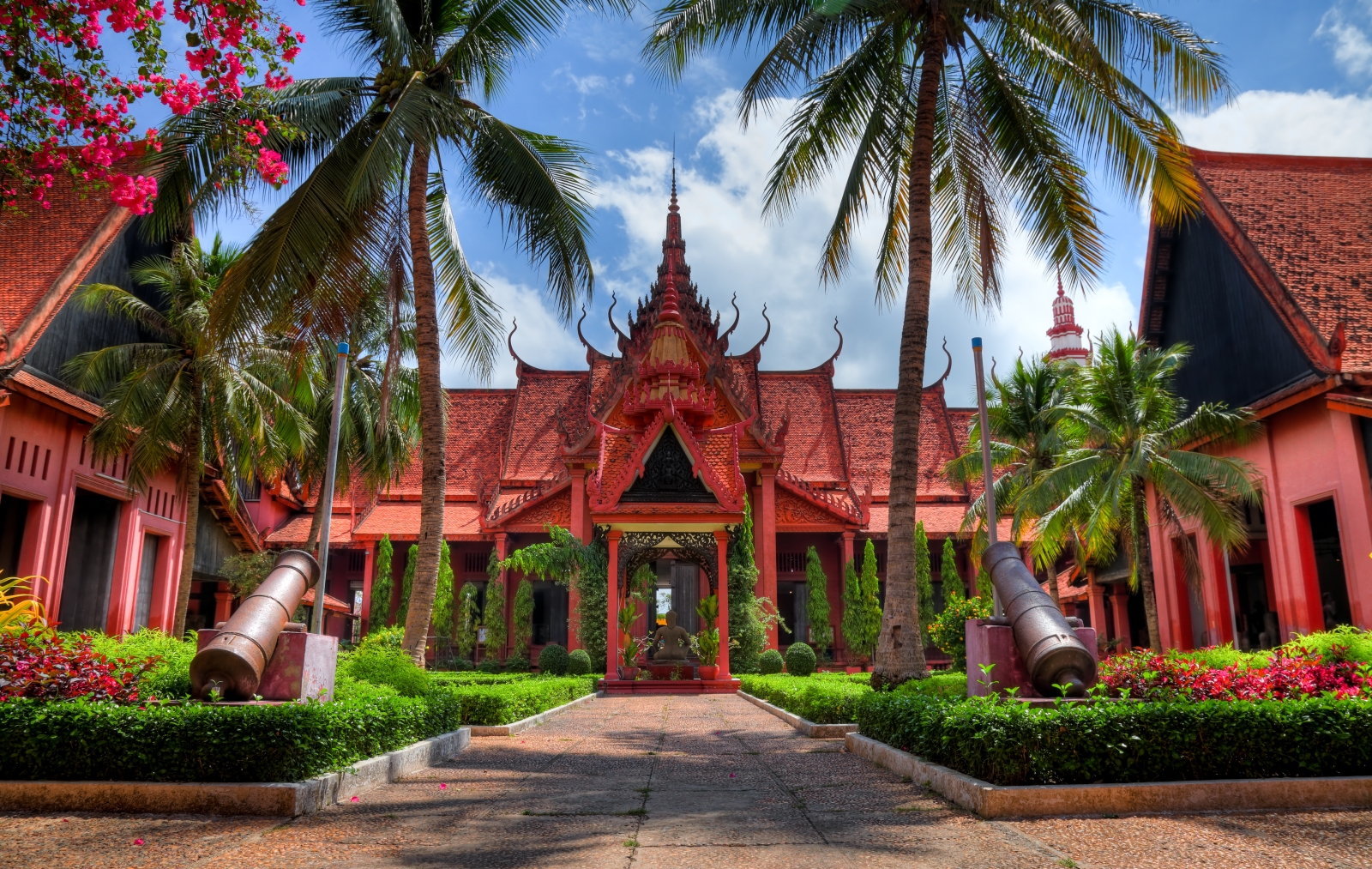 Red bricked building with ornate designs, palm trees line the path