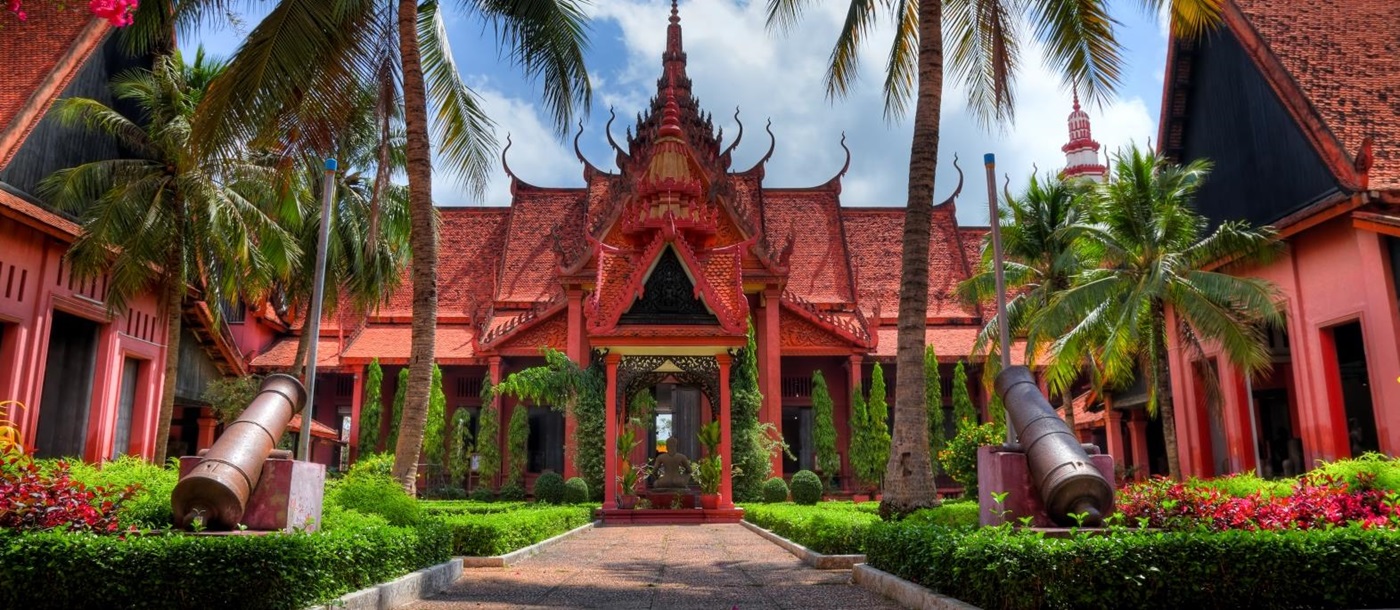 Red bricked building with ornate designs, palm trees line the path