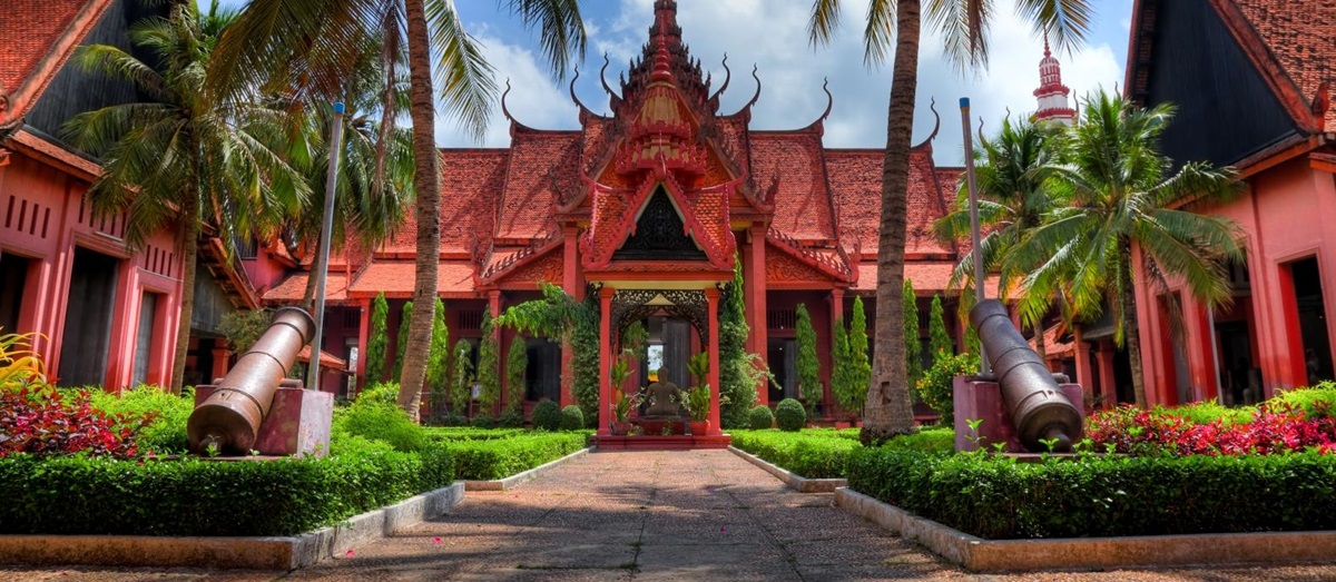 Red bricked building with ornate designs, palm trees line the path