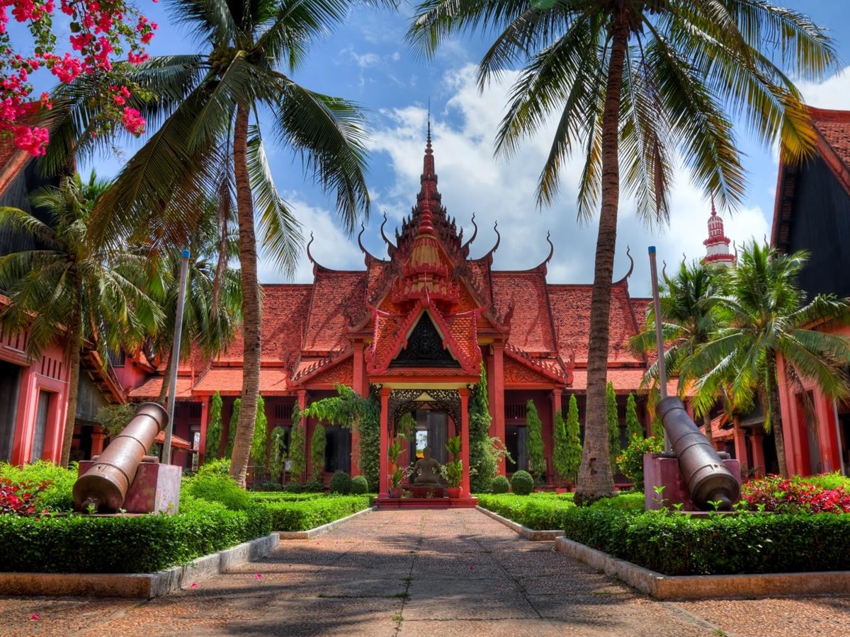 Red bricked building with ornate designs, palm trees line the path