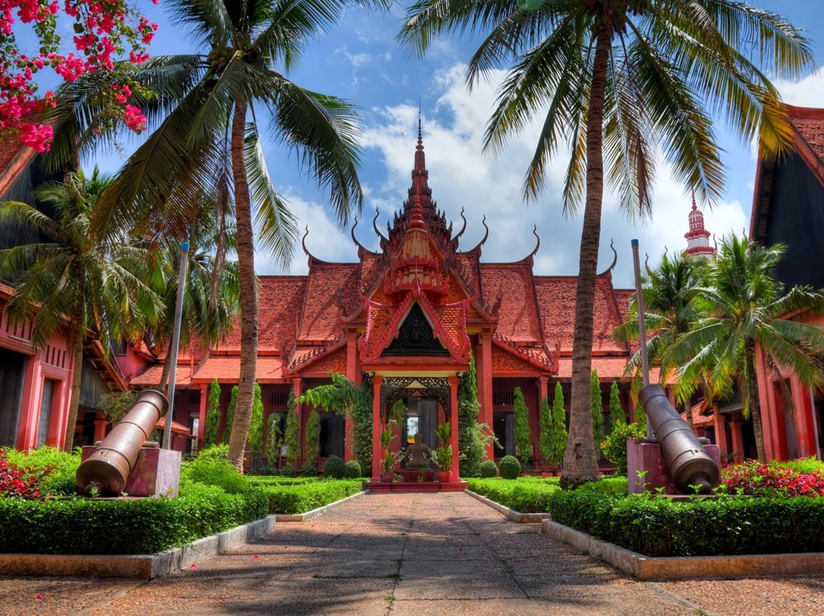 Red bricked building with ornate designs, palm trees line the path