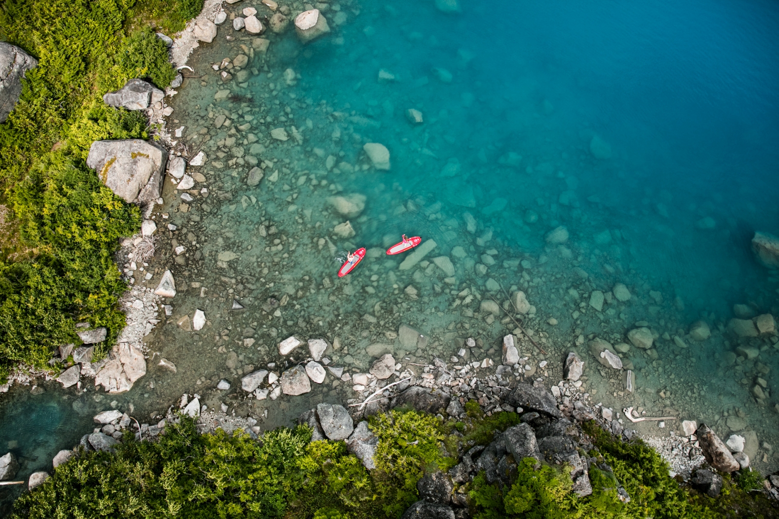Two guests on stand up paddleboards in a bay with turquoise water near luxury hotel Nimmo Bay in Canada