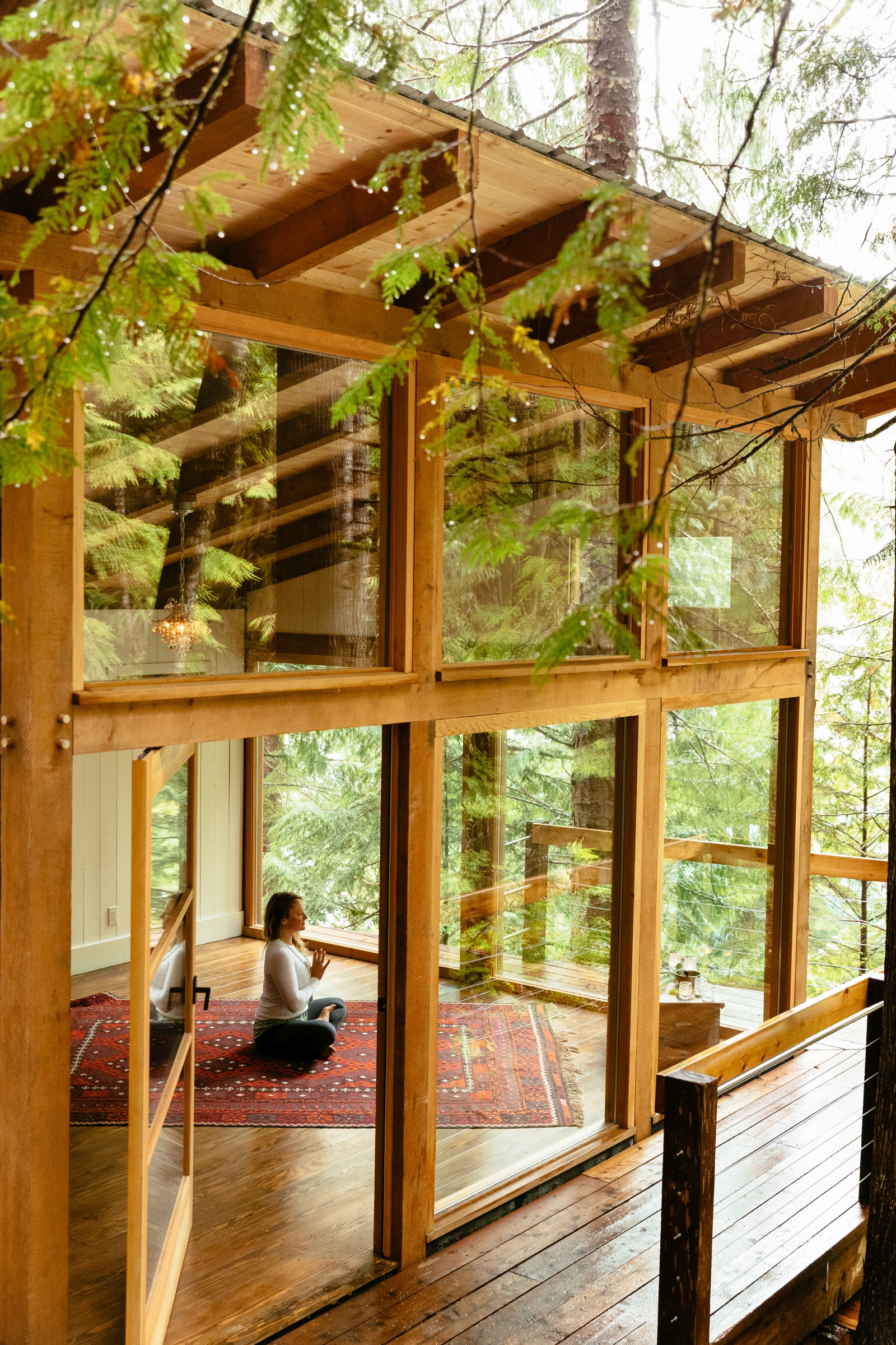 Guest meditating in a glass-walled yoga pavilion in the lush green foret at luxury hotel Nimmo Bay in Canada
