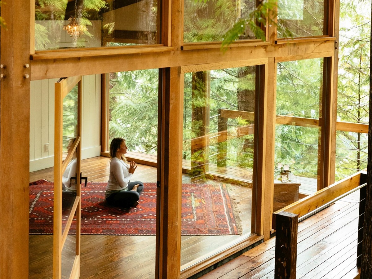 Guest meditating in a glass-walled yoga pavilion in the lush green foret at luxury hotel Nimmo Bay in Canada