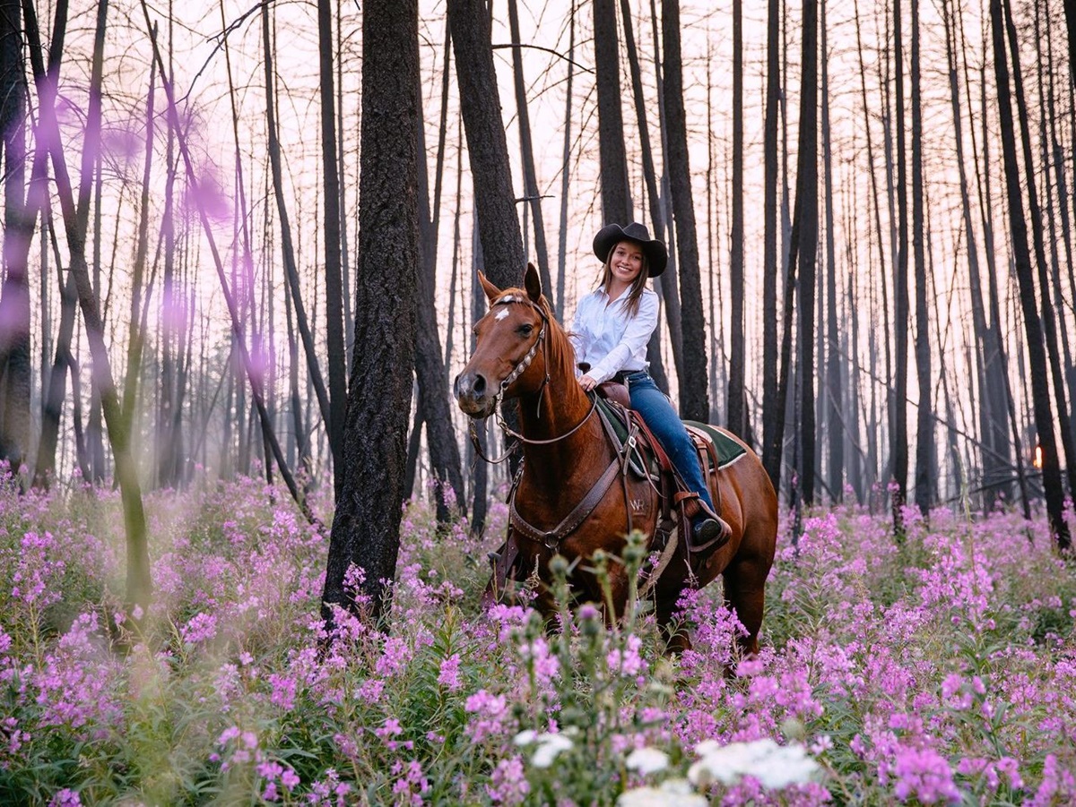 A gust riding a horse through a flowery forest on the grounds of Siwash Lake Ranch in Canada's British Columbia
