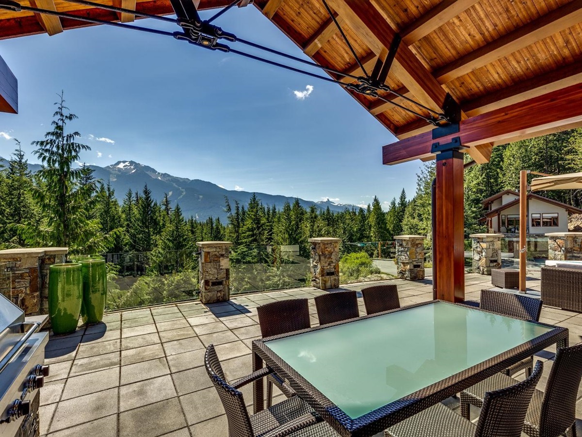 Covered terrace with outdoor dining and BBQ overlooking the mountains at luxury private home The Belmont Estate in Whistler, Canada