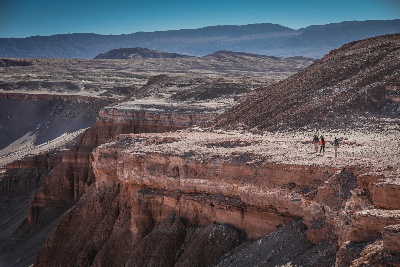 Three hikers walking along a rift in the lunar-like landscape