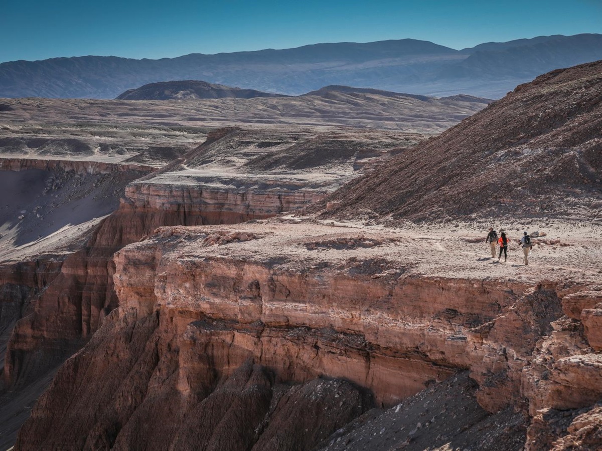 Three hikers walking along a rift in the lunar-like landscape