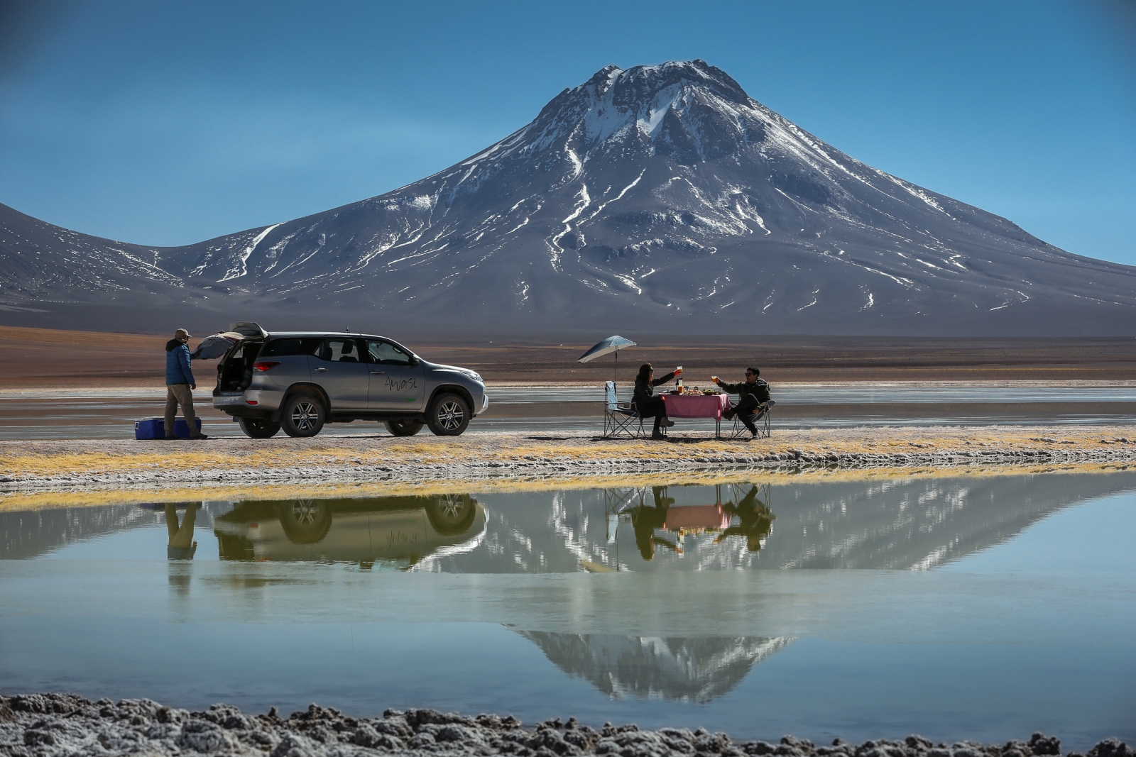 Two people enjoying lunch by a lake with snowy mountain in the background