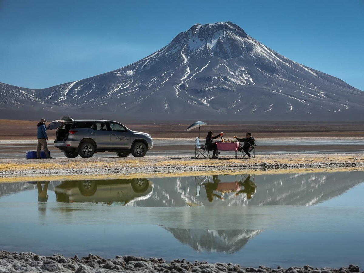 Two people enjoying lunch by a lake with snowy mountain in the background