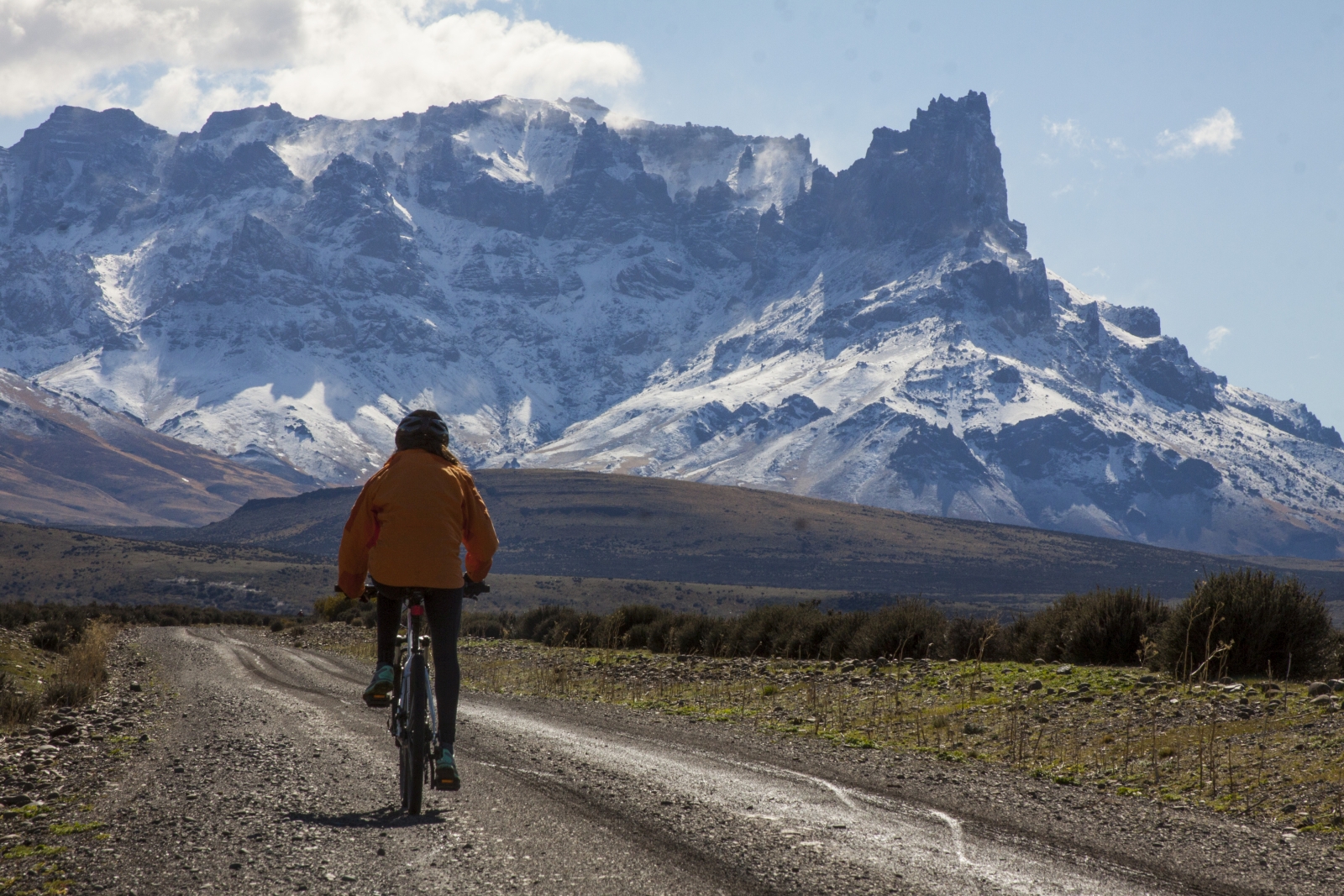 Cyclist riding towards snowy mountains